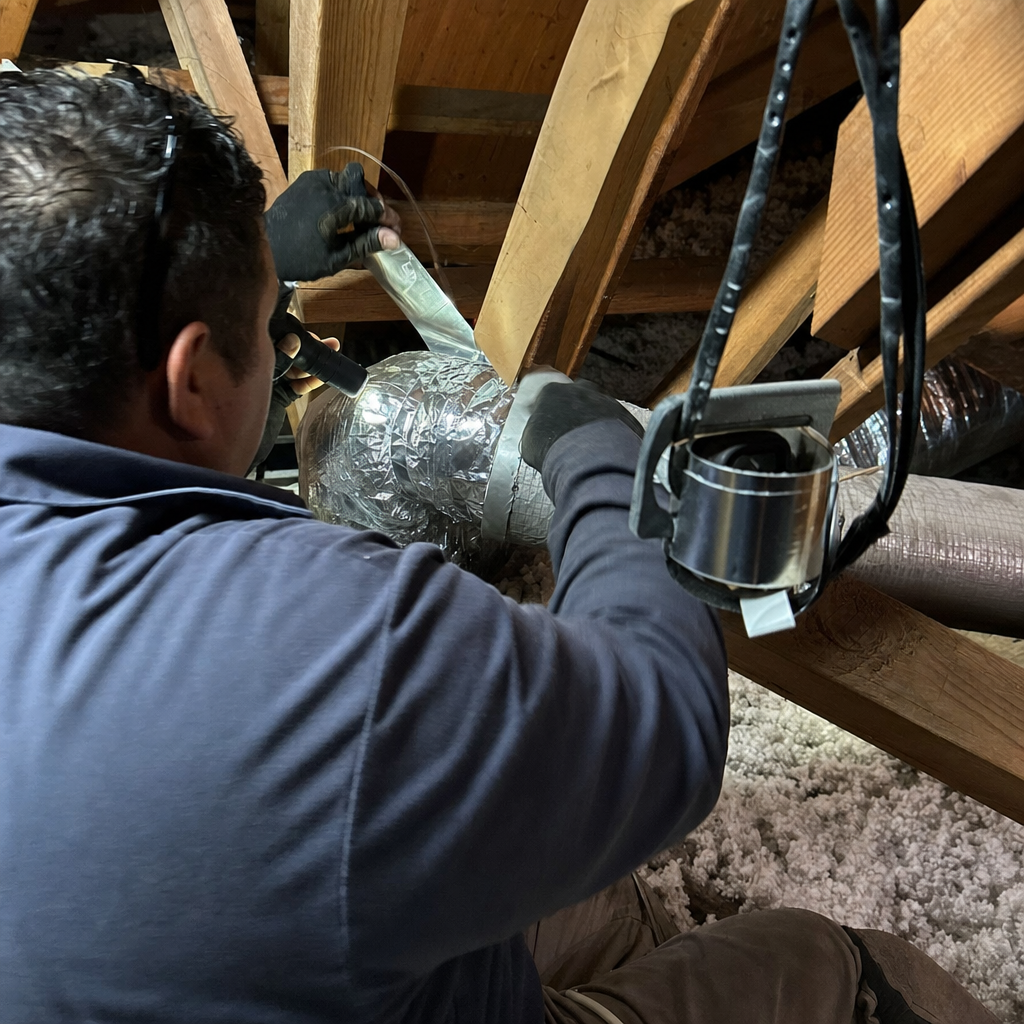 Technician repairing and sealing flexible air duct in attic